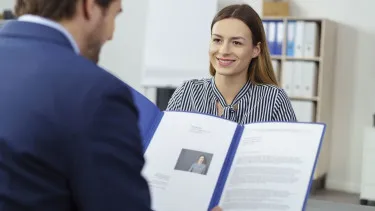Eine Nahaufnahme zeigt ein Bewerbungsschreiben und eine Hand, die einen Stift hält, um wichtige Details zu markieren.