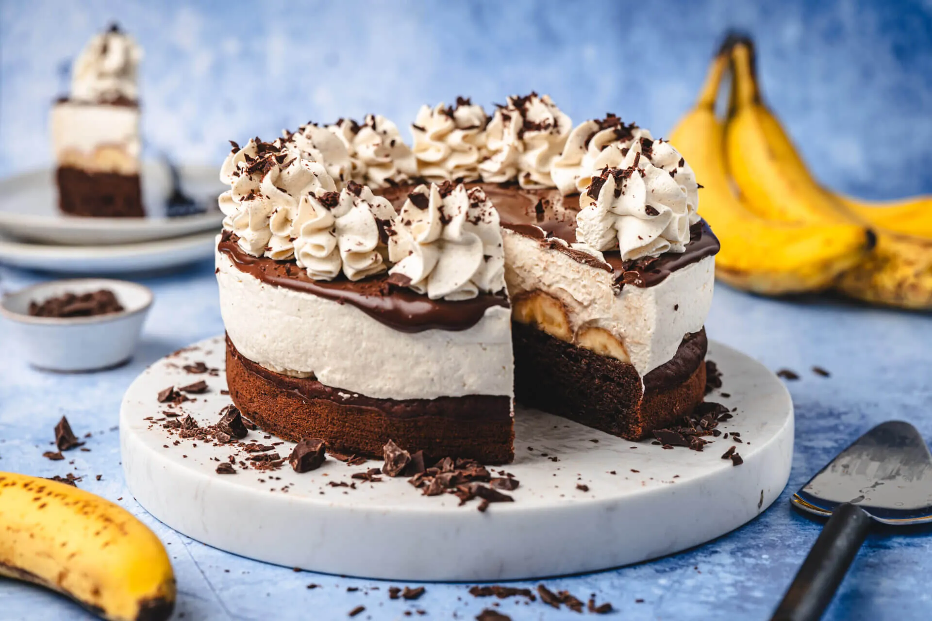 Eine perfekt angeschnittene Schoko Bananen Sahne Torte auf blauem Hintergrund mit Bananen