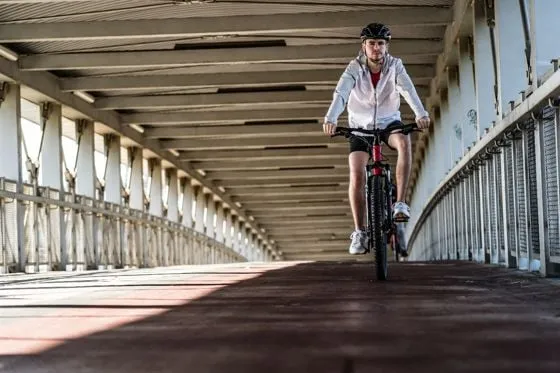 Eine Person fährt ein Fahrrad auf einer Brücke. Sie trägt sportliche Kleidung und einen Helm.