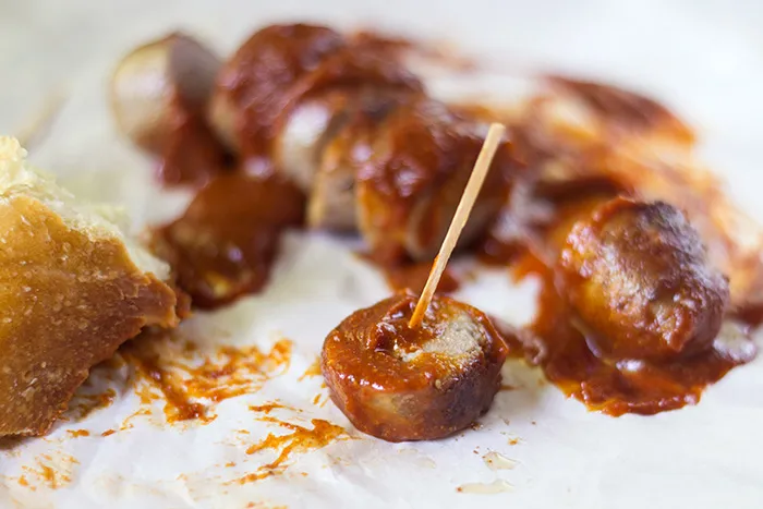 Eine Pfanne mit gebratenen Bratwürsten und einer Schüssel voller hausgemachter Currywurst-Soße