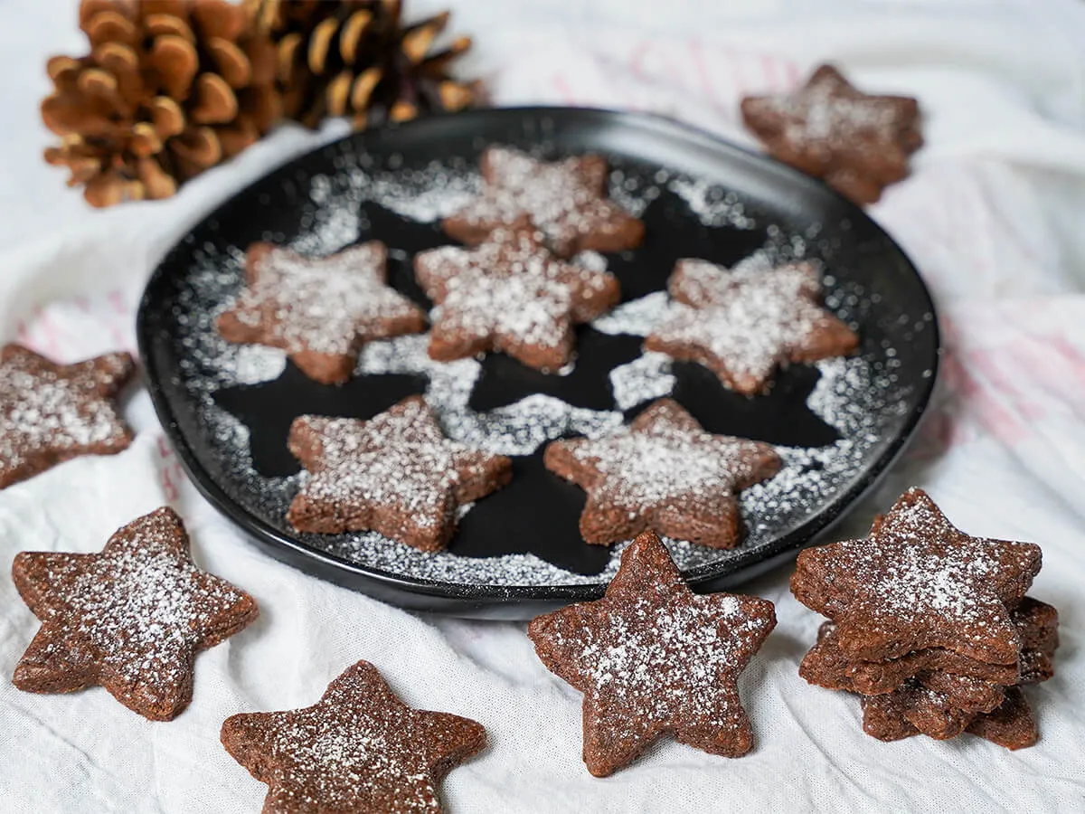 Eine Platte mit Basler Brunsli Schokoladen-Mandel-Keksen, teilweise auf einem Tuch um die Platte angeordnet.