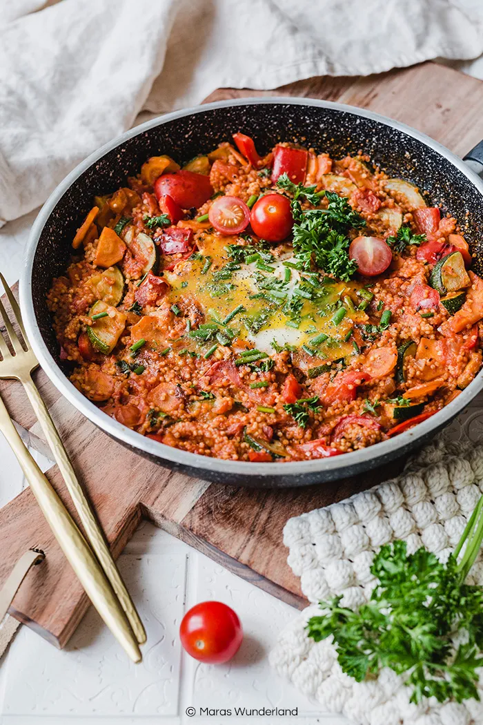 Eine Portion Hirse-Shakshuka in einer Schale, garniert mit frischen Kräutern und einem Löffel