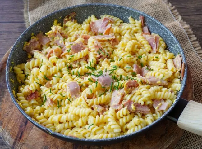 Eine Portion Schinkennudeln mit Rührei und frischen Kräutern auf einem weißen Teller