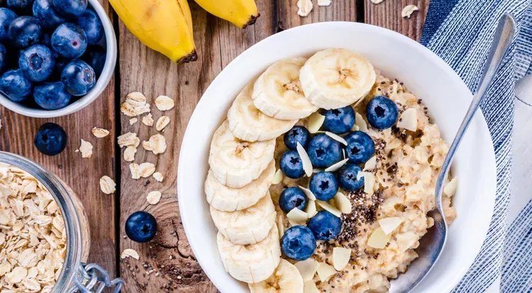 Eine Schale mit cremigem Protein-Porridge, reichlich belegt mit frischen Bananenscheiben, Heidelbeeren und Mandelstiften.