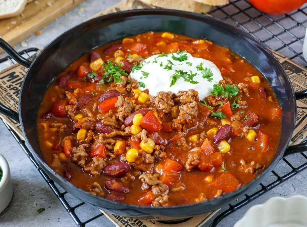 Eine Schüssel mit herzhaftem Chili con Carne, garniert mit frischen Kräutern und einem Klecks Sauerrahm