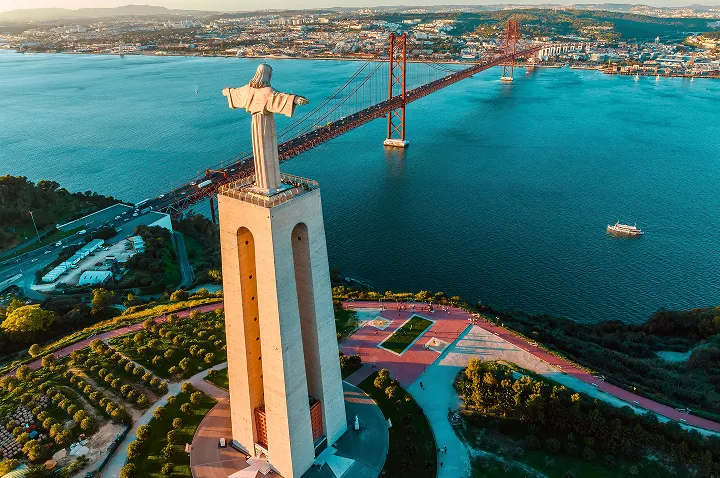 Eine Statue von Jesus steht majestätisch auf einem Hügel in Lissabon, umgeben von einer malerischen Landschaft.
