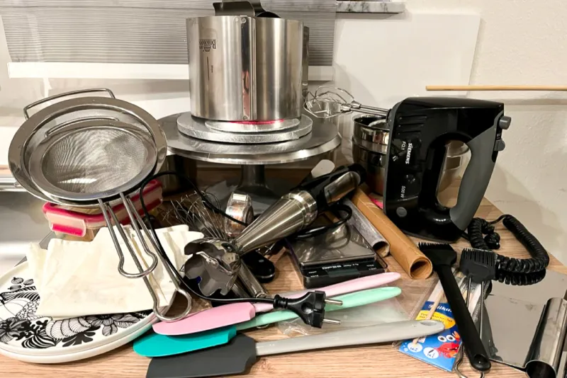 Eine Vielzahl von Backutensilien, die für die Zubereitung einer zweistöckigen Hochzeitstorte benötigt werden, inklusive Schüsseln, Backformen und Werkzeugen.