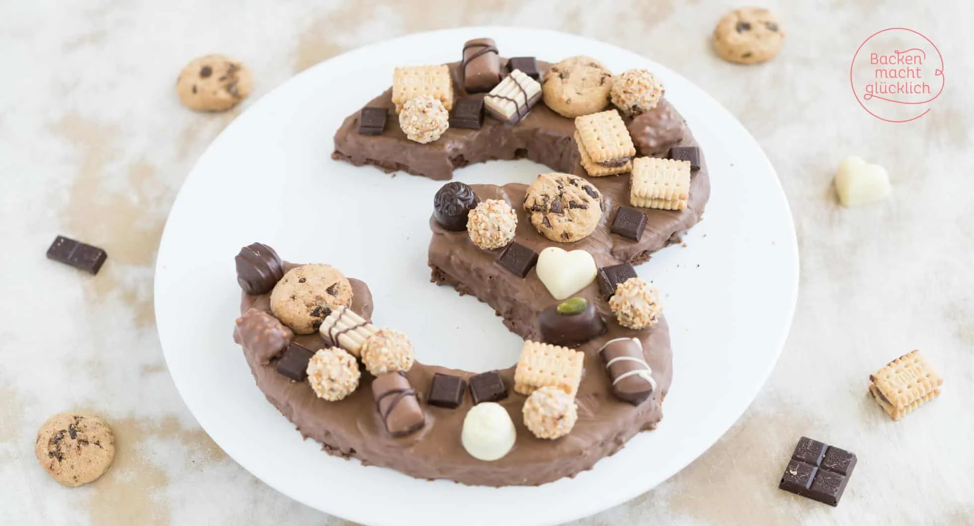 Eine wunderschön dekorierte Zahlentorte in Form der Zahl 3, verziert mit Schokolade, Mini-Pralinen und Cookies.