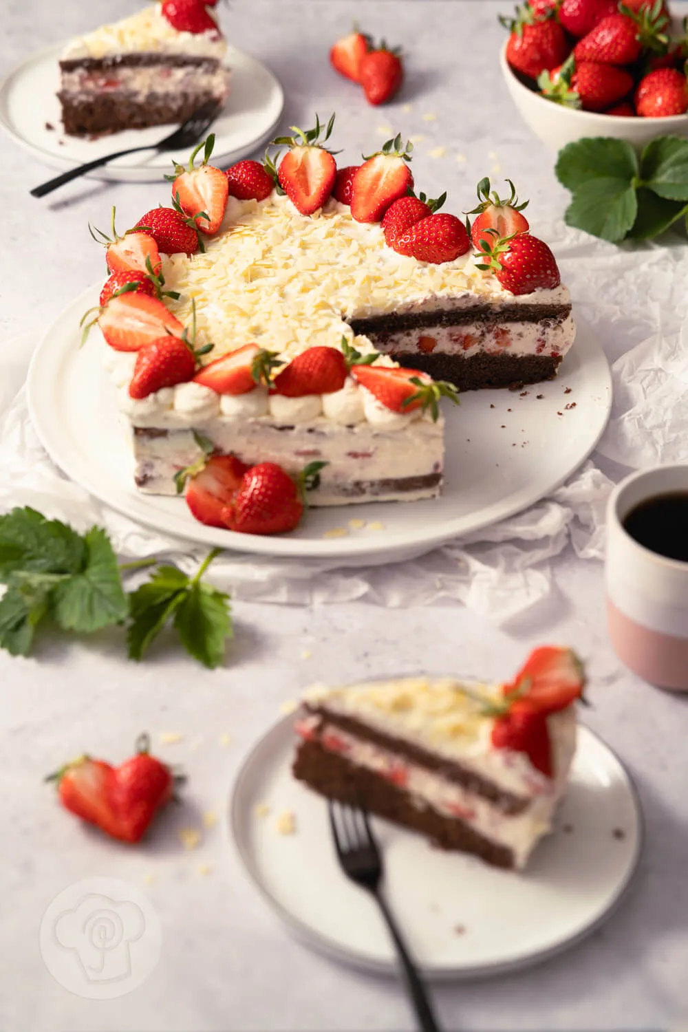 Einfache Erdbeertorte in Herzform auf einem Teller, angeschnitten. Kuchenstücke auf Tellern