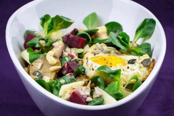 Fertig angerichteter Topinambur-Salat mit gebratenem Spiegelei, Äpfeln, Roter Bete und Kernen, bereit zum Servieren