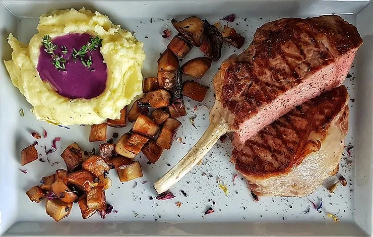 Fertig angerichtetes Kalbskotelett mit lila Sauce, Kräuterseitlingen und Kartoffelpüree