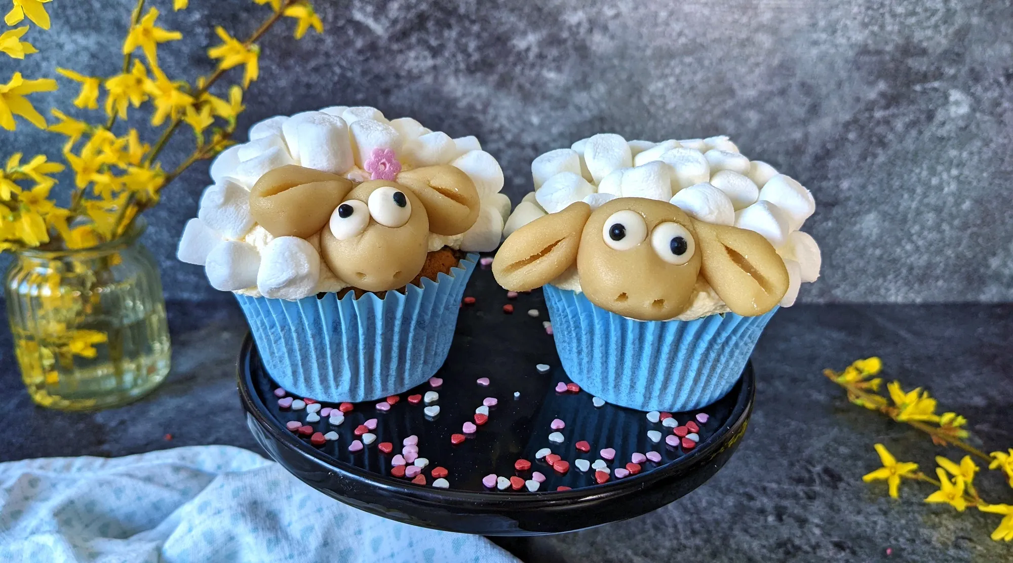 Fertig dekorierte Schaf-Muffins mit bunten Streuseln auf einer blauen Oberfläche