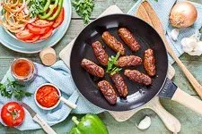 Fertig gebratene Cevapcici, perfekt angerichtet mit frischen Beilagen wie Ajvar und Zwiebeln