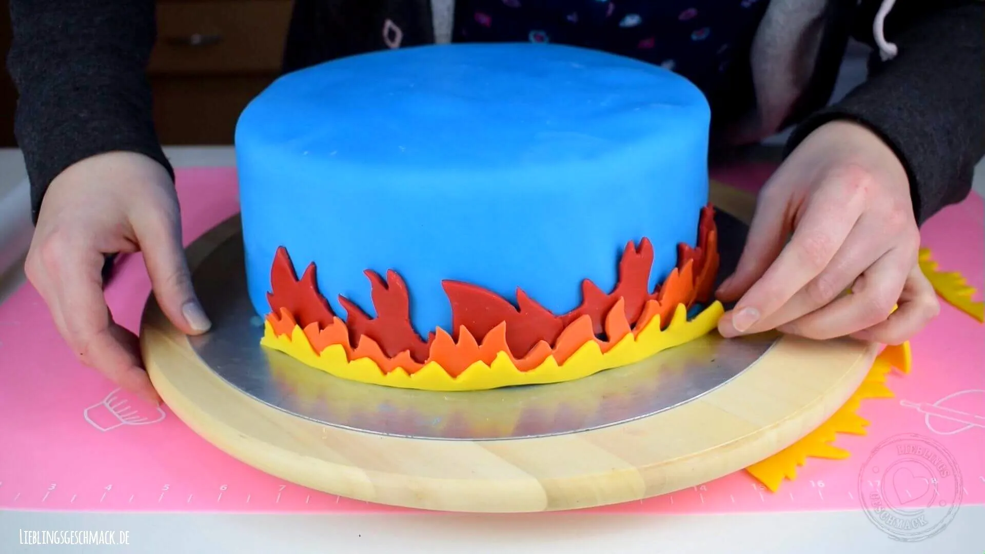 Flammenband aus bunten Fondantstreifen wird um die Torte geklebt.