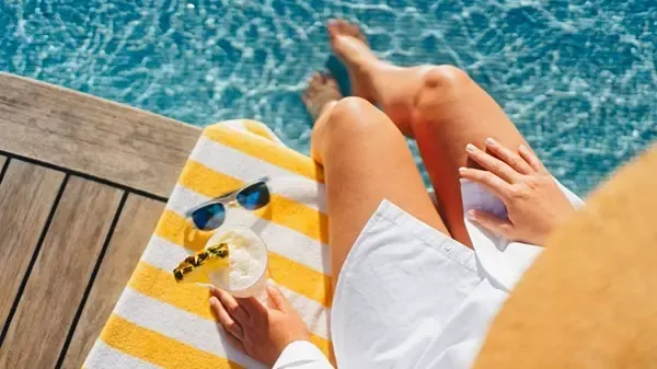Frau am Pool mit Sonnenbrille und Handtuch