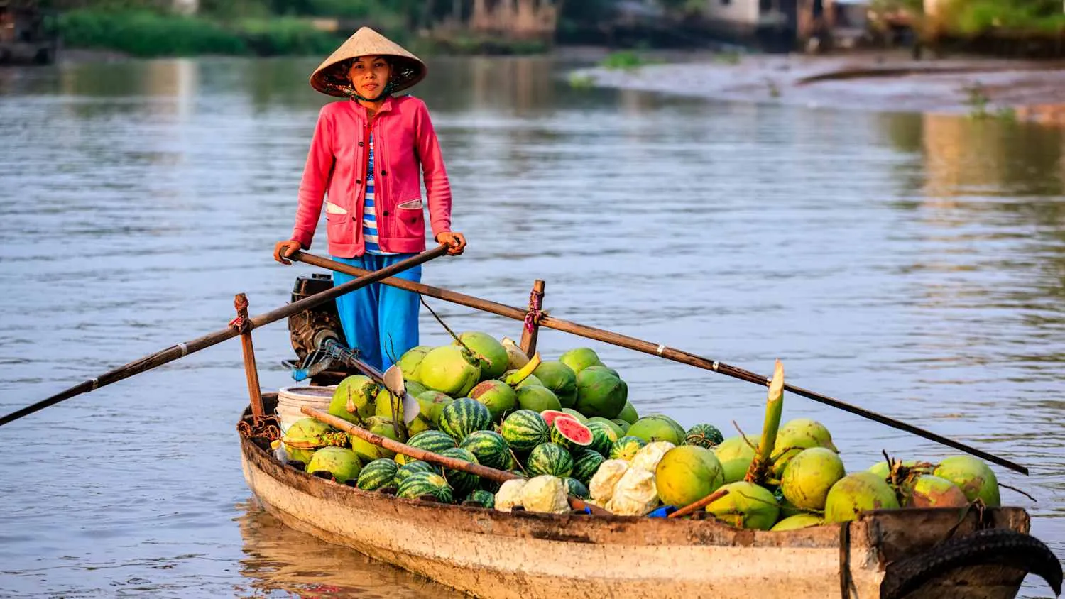 Frau fährt mit Boot voller Wassermelonen und Kokosnüsse auf dem Mekong in Vietnam