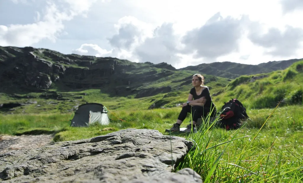 Frau zeltet alleine in der Wildnis mit Blick auf eine malerische Berglandschaft