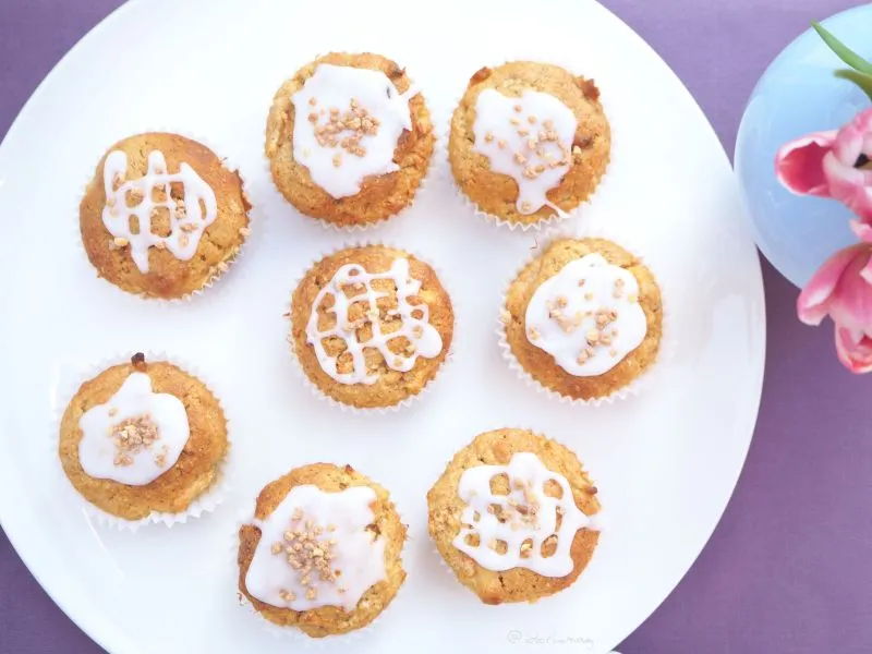 Frisch gebackene Apfel-Karotten-Nuss-Muffins mit knuspriger Oberfläche in Papiermanschetten auf einem Holzbrett