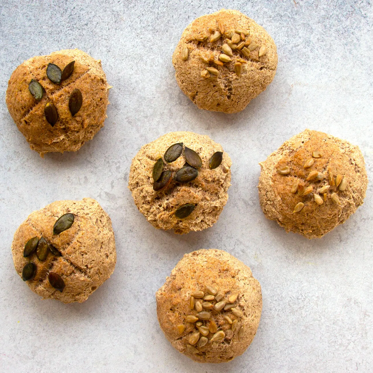 Frisch gebackene, goldbraune Buchweizenbrötchen auf einem Backblech, bestreut mit Kürbis- und Sonnenblumenkernen