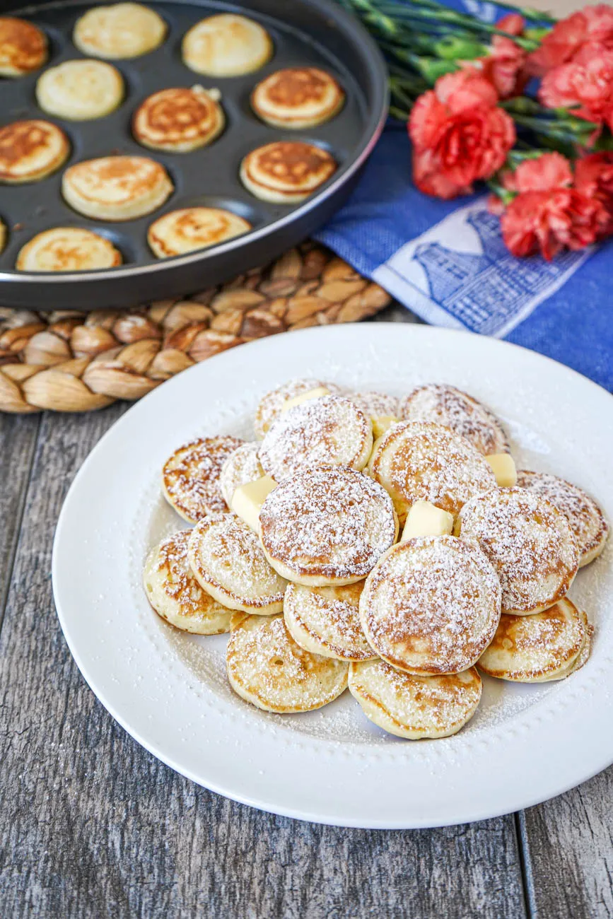 Frisch gebackene Poffertjes (Holländische Mini-Pfannkuchen) mit geschmolzener Butter und reichlich Puderzucker bestreut, bereit zum Genießen.