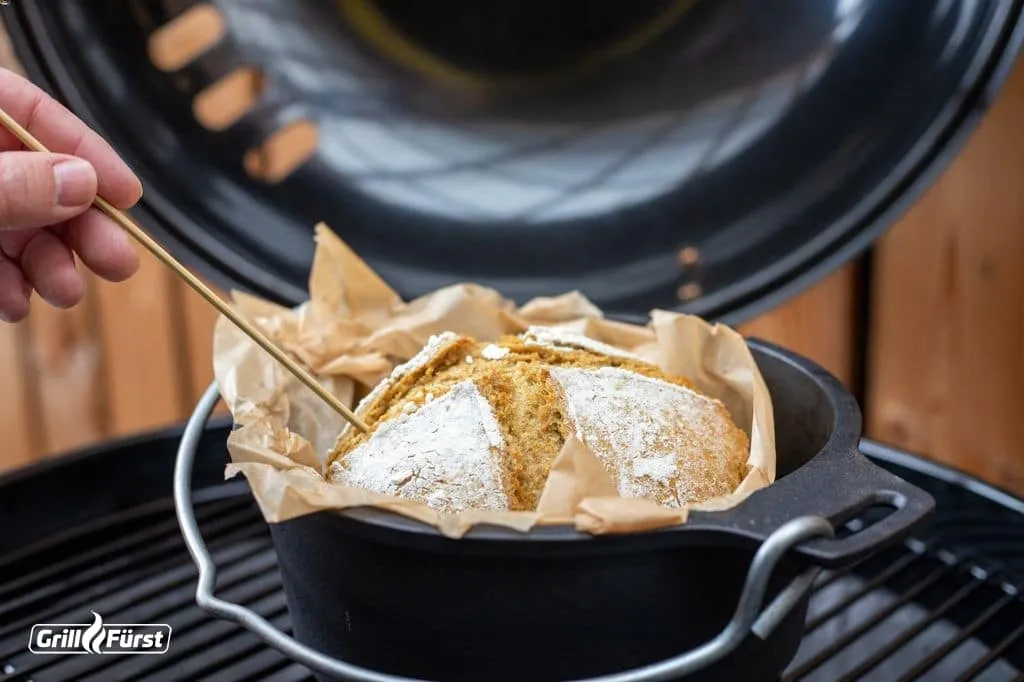 Frisch gebackenes Brot im Dutch Oven, umgeben von glühenden Kohlebriketts