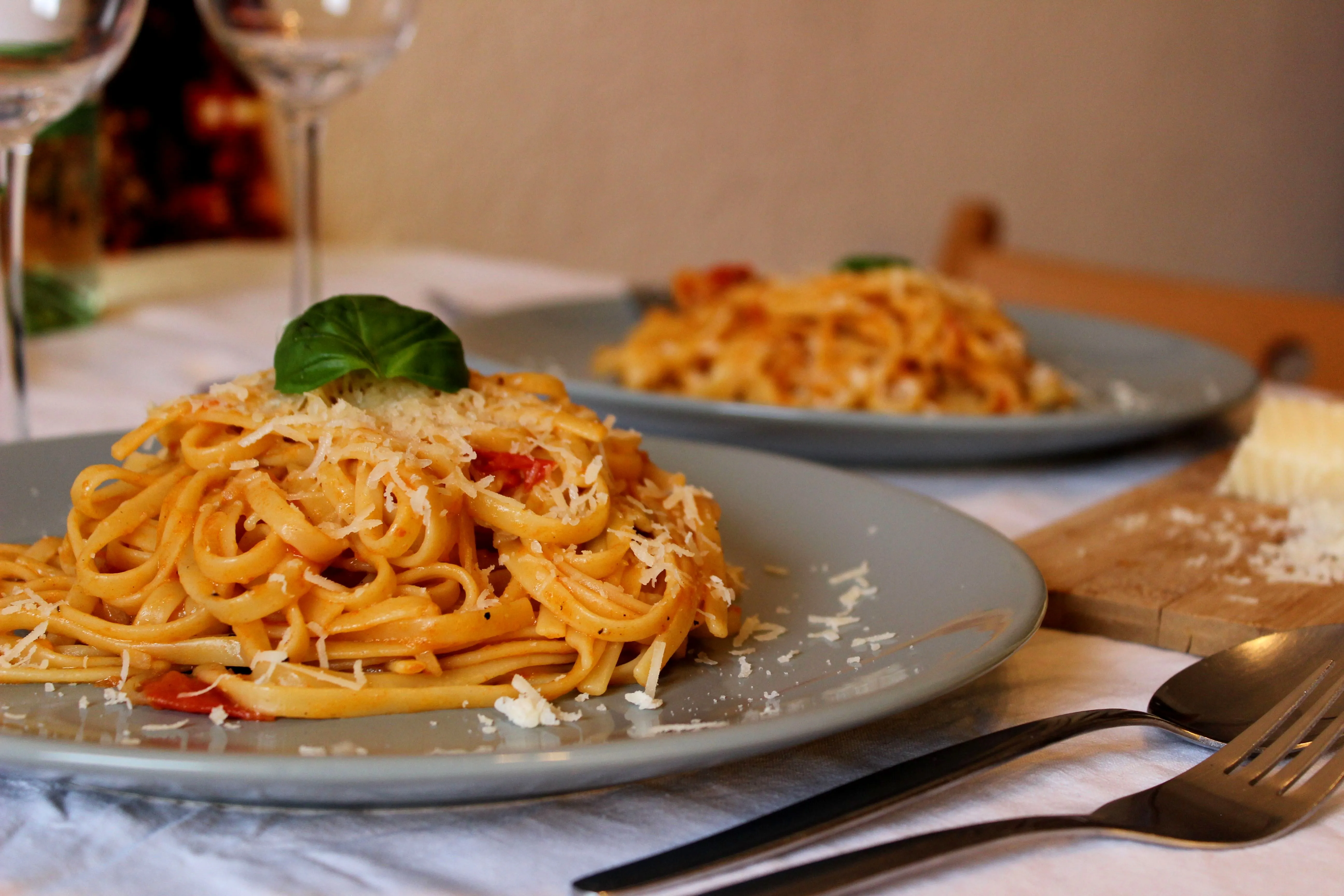 Frische Linguine, halbierte Kirschtomaten, Zwiebeln und Basilikum in einer großen Pfanne vor dem Kochen