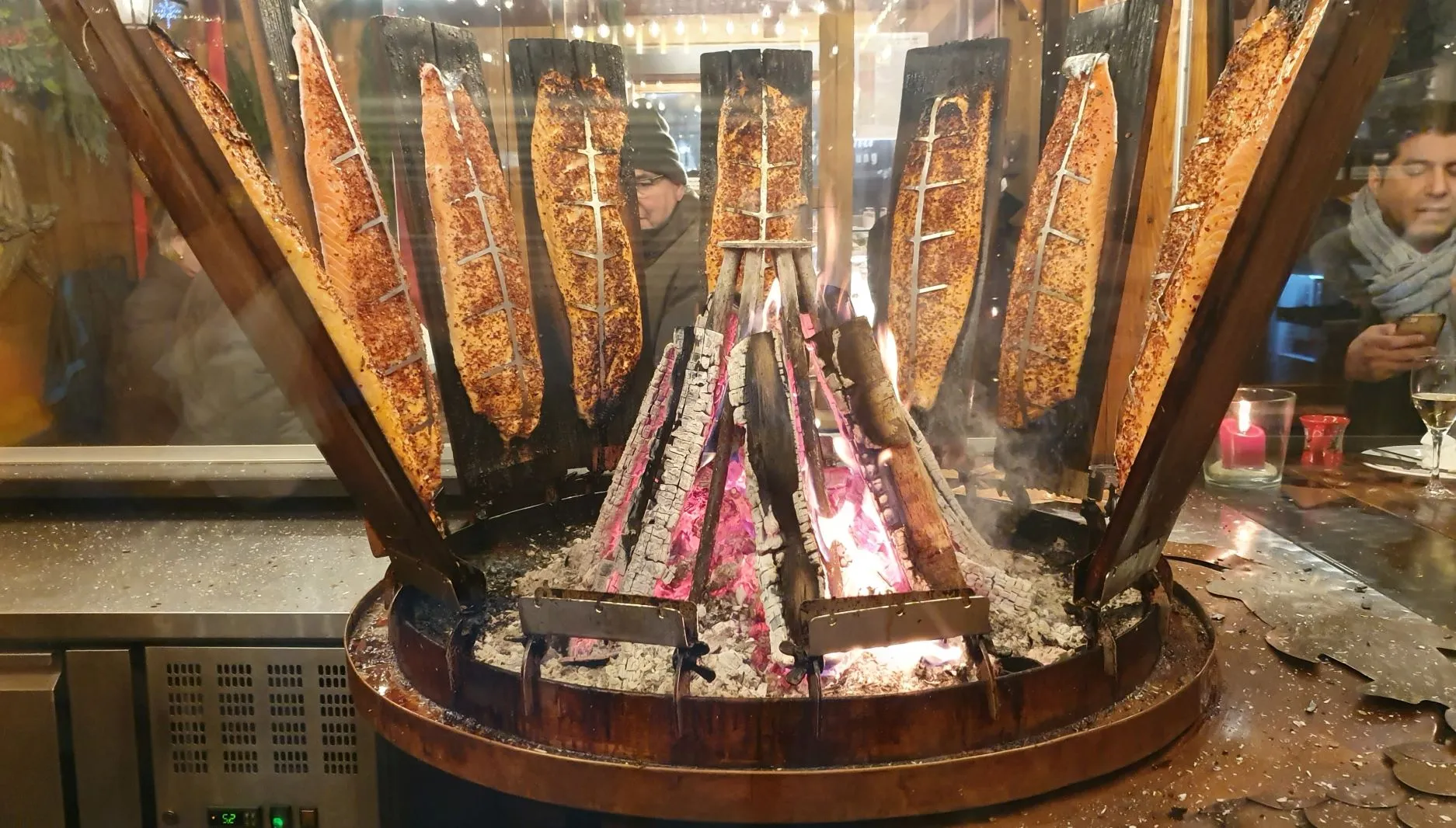 Frischer Flammlachs auf einem Holzbrett gart langsam über offenem Holzfeuer