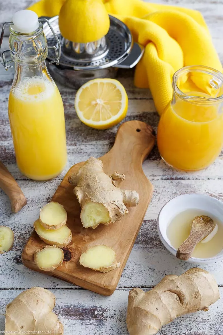 Frischer Ingwer, Zitronen und Orangen liegen bereit auf einer Holzoberfläche als Zutaten für den Ingwer-Shot