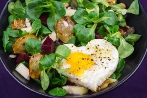 Frischer Topinambur-Salat mit Apfel, Roter Bete und einem perfekt gebratenen Spiegelei auf rustikalem Teller