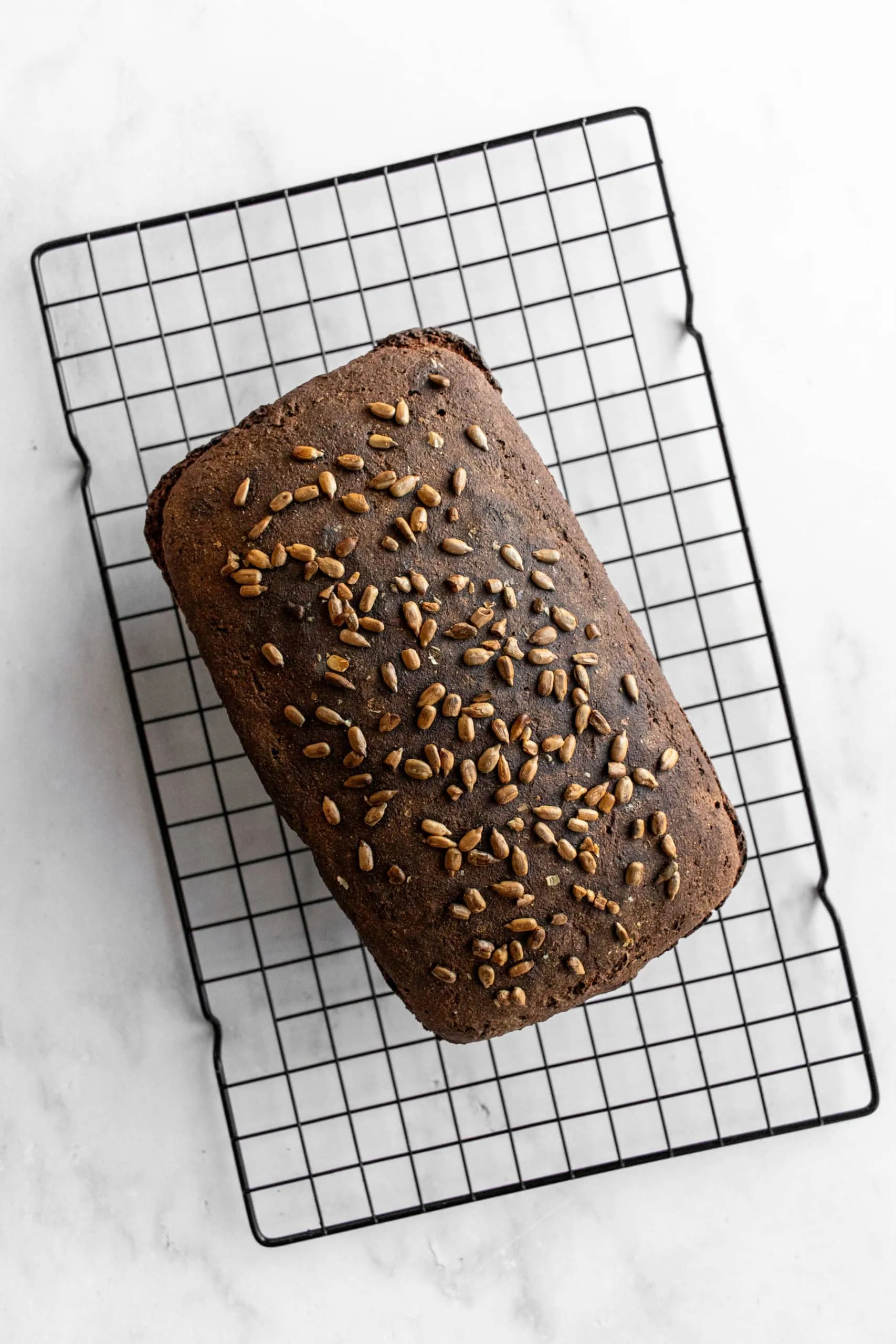 Gebackener Laib Schwarzbrot mit Sonnenblumenkernen auf einem Kuchengitter.