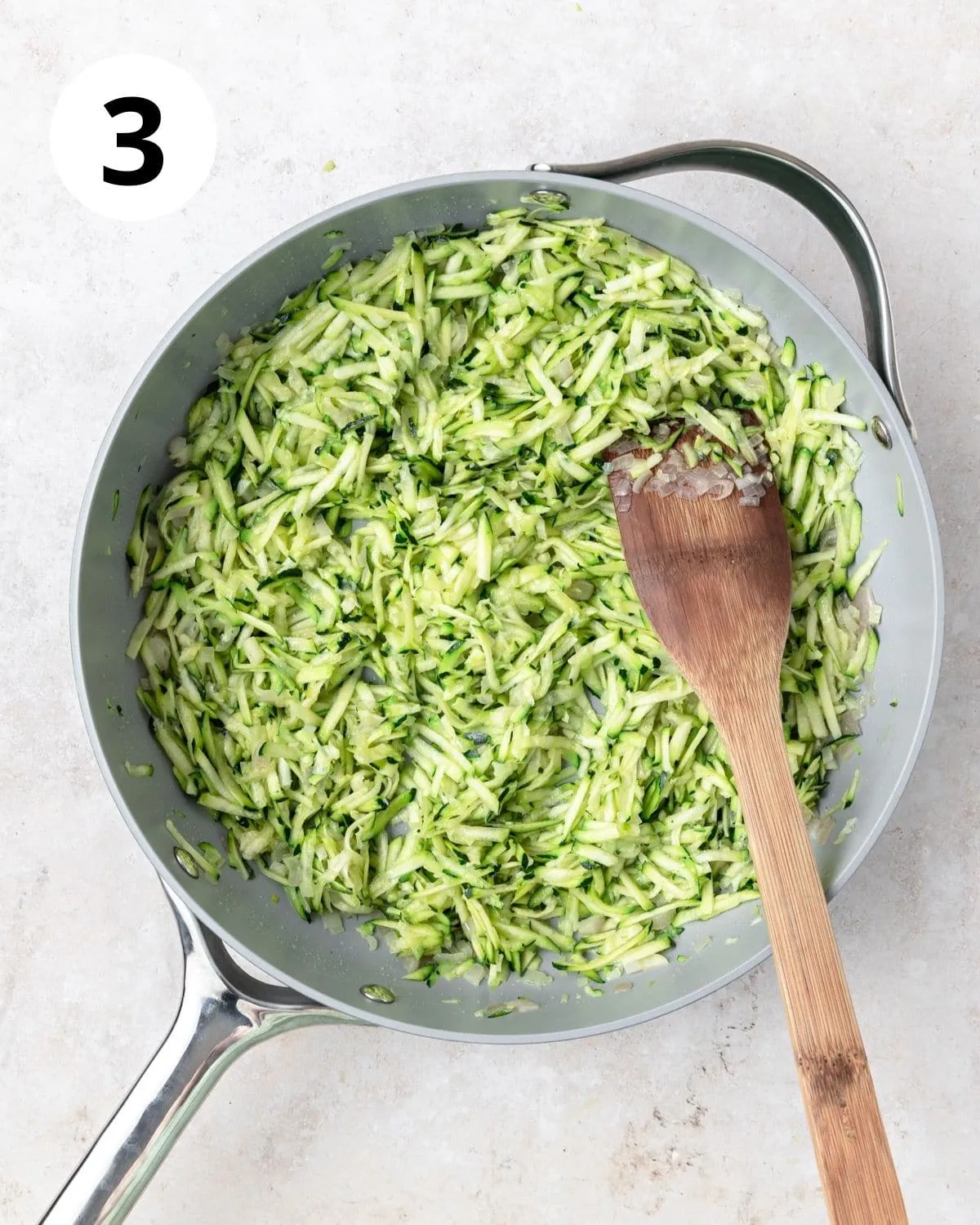 Geriebene Zucchini zu einer großen Pfanne hinzufügen