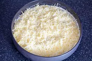 Geriebener Käse wird gleichmäßig über die Kartoffelschichten und die cremige Sauce verteilt
