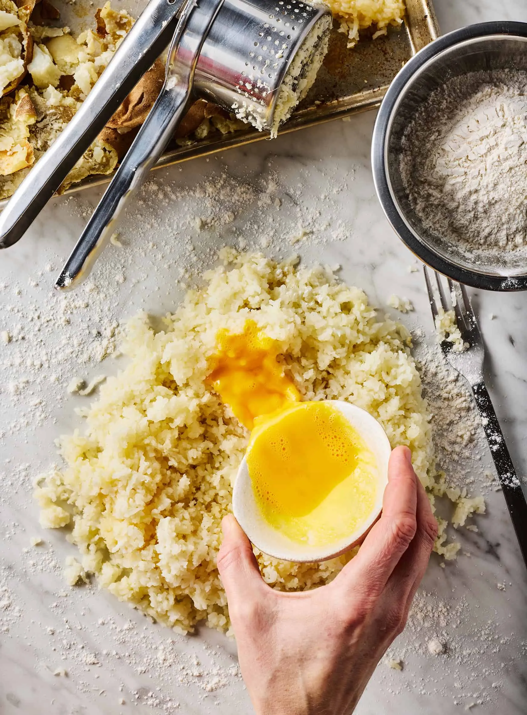 Geschlagenes Ei wird über die gepressten Kartoffeln auf einer bemehlten Fläche gegossen