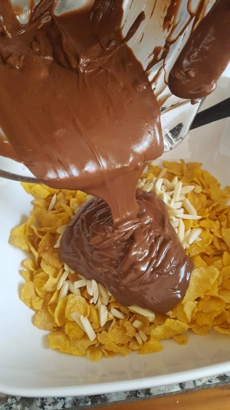 Geschmolzene Schokolade wird über die Cornflakes und Mandeln gegossen