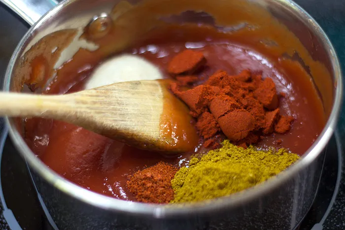 Gewürze wie Currypulver und Paprika werden zu dem Ketchup in einem Topf hinzugefügt