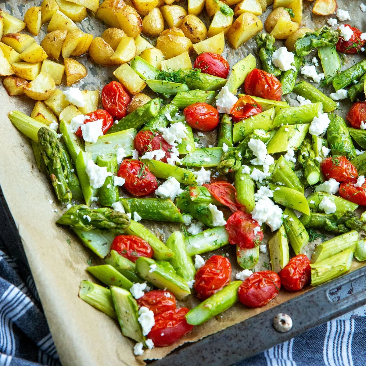 Großaufnahme eines Tellergerichts mit grünem Spargel, Kartoffeln und Tomaten aus dem Ofen