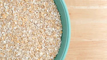 Haferkleie in einer hellen Schüssel mit einem Holzlöffel, bereit zum Verzehr