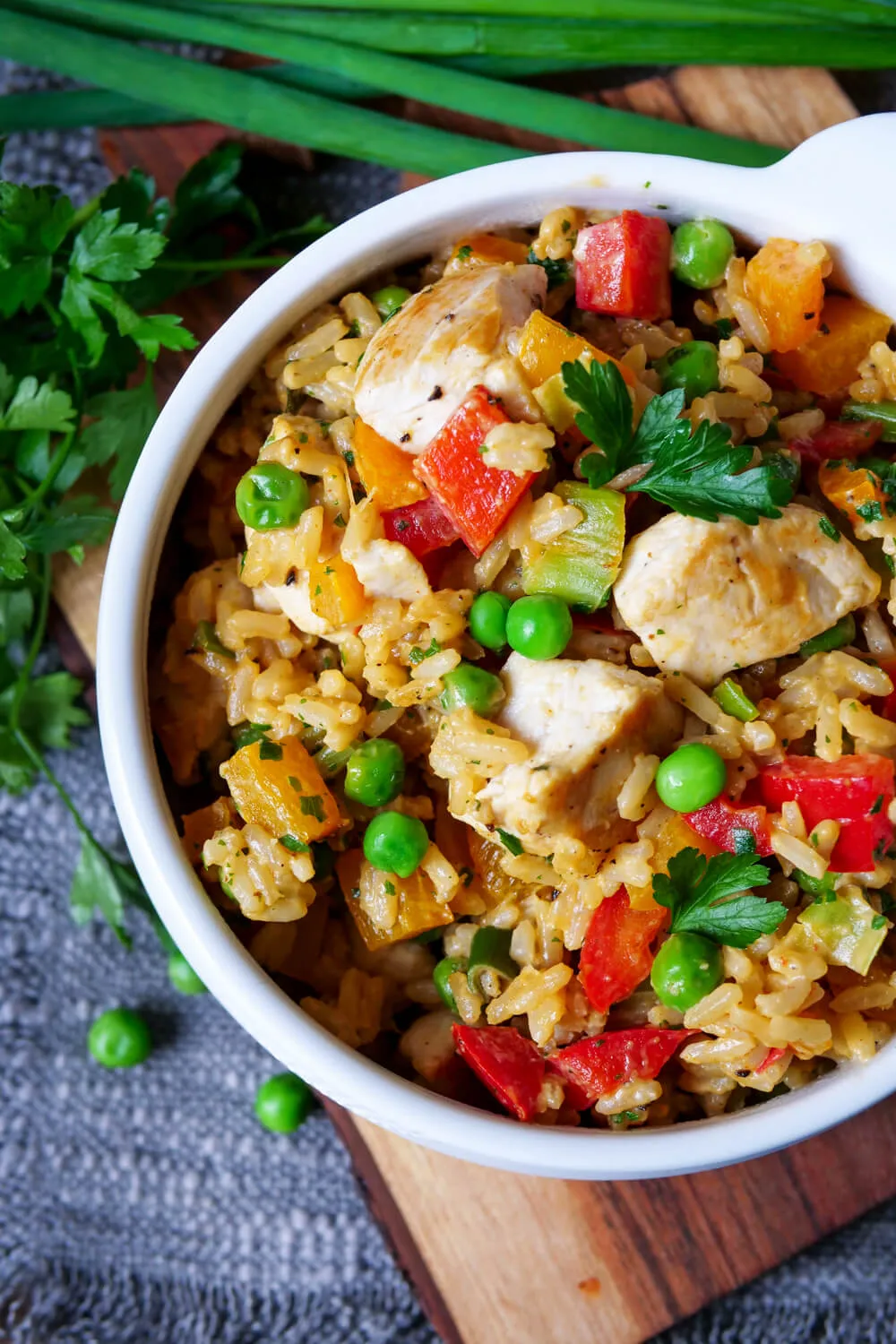 Hähnchen-Reis-Pfanne mit Paprika, Frühlingszwiebeln, Erbsen und Petersilie garniert