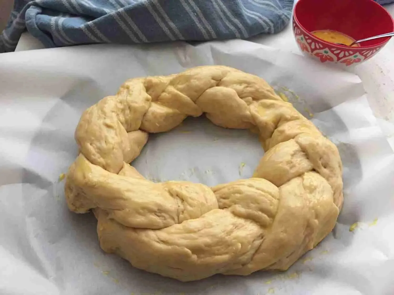 Hände bestreichen den ungebackenen Hefezopf sorgfältig mit einer Eigelb-Milch-Mischung