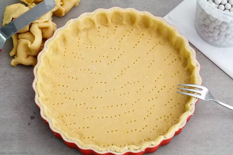 Hände, die Mürbeteig in einer Quicheform auslegen