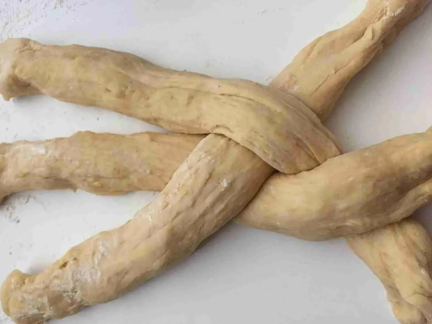 Hände flechten geschickt drei Teigstränge zu einem schönen Zopf, beginnend in der Mitte