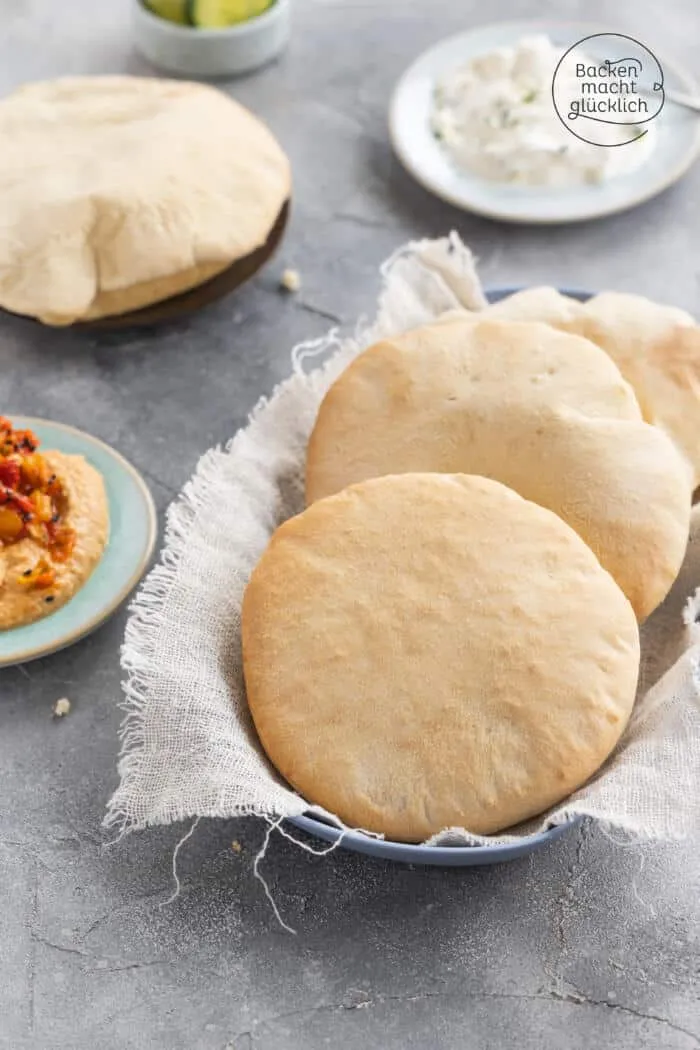 Hände rollen Hefeteig für Pita-Brot auf einer bemehlten Arbeitsfläche aus