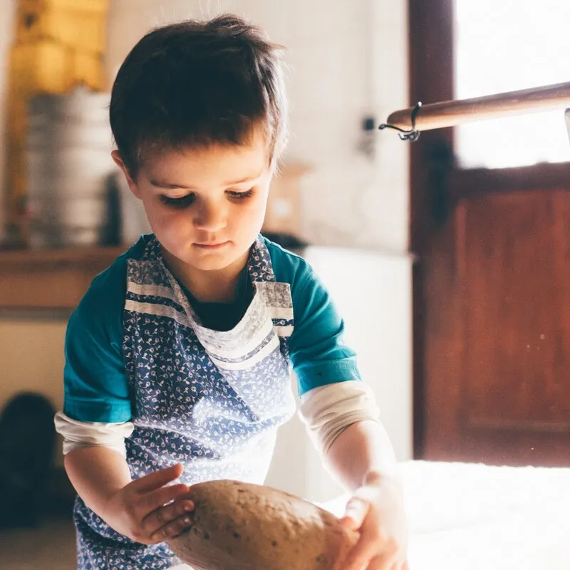 Kind nimmt frisches Brot von einem Backblech in einer Bauernküche.
