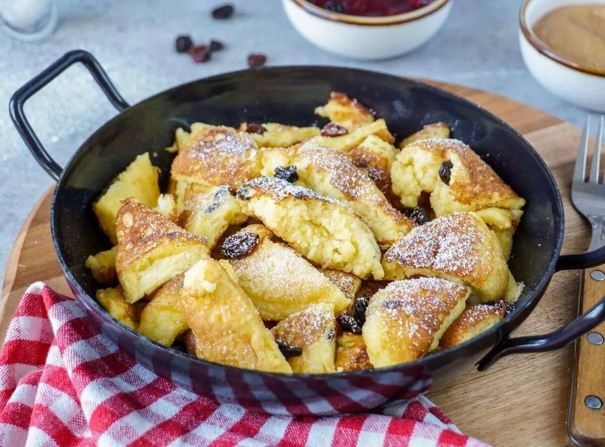 Luftiger Kaiserschmarrn mit Puderzucker bestreut, serviert mit Apfelmus auf einem rustikalen Holztisch