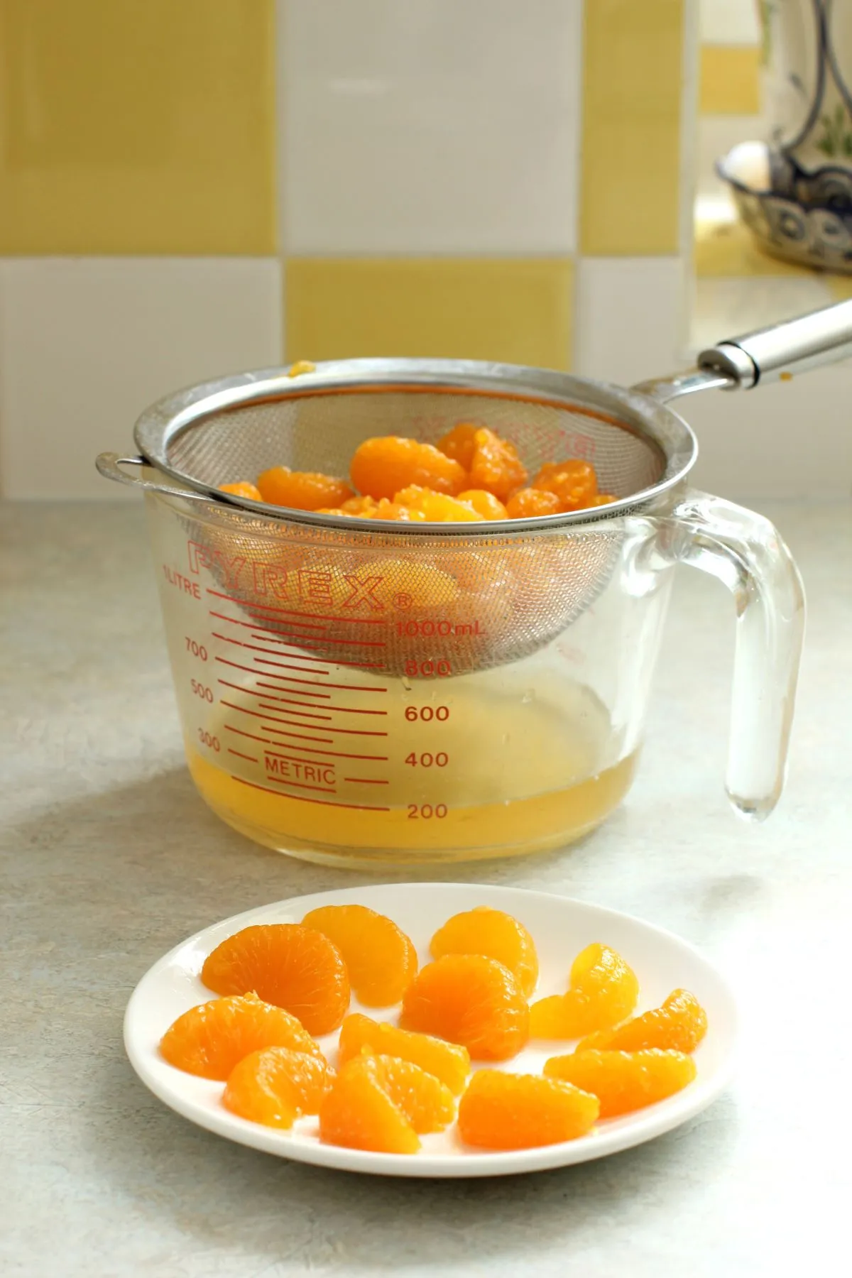 Mandarinenstücke in einem Sieb über einem Messbecher. Kleine Schale mit Mandarinenfilets davor.