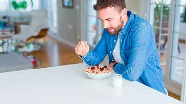 Mann genießt ein gesundes Frühstück mit Müsli, Beeren und Haferkleie in einer Schale