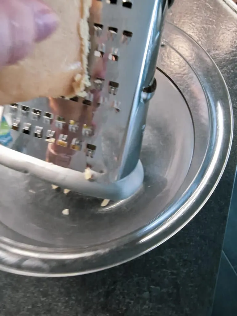 Marzipanrohmasse wird mit einer Vierkantreibe grob gerieben, um es für den Marzipankuchen vorzubereiten