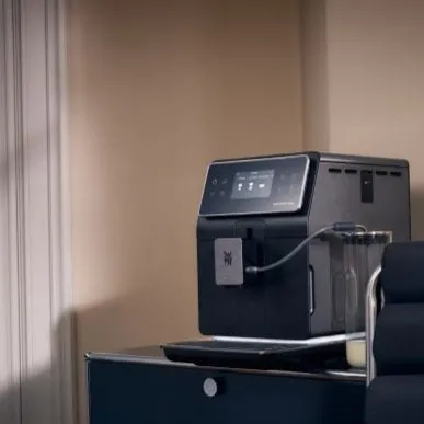 Moderne schwarze Kaffeemaschine mit Touchdisplay und Milchaufschäumer auf einem Tisch in heller Küche.