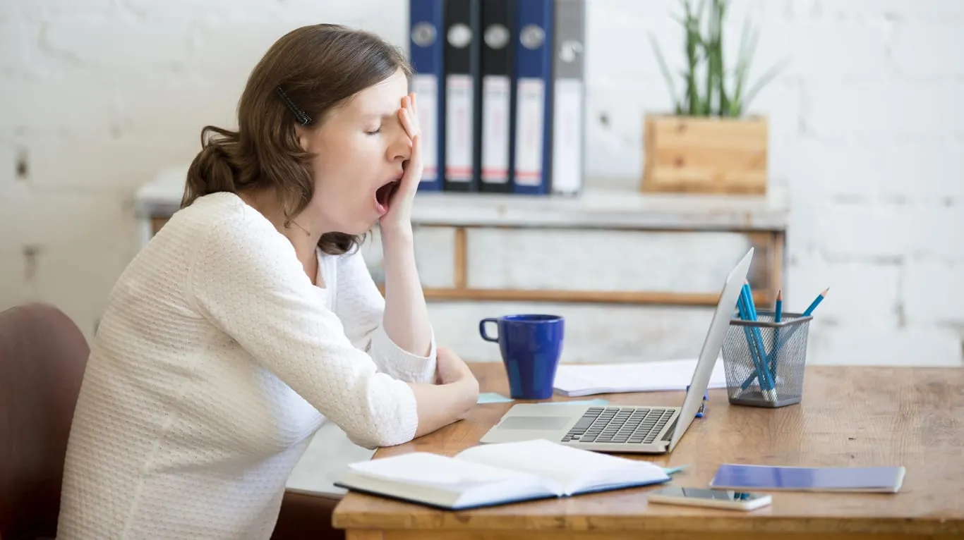 Müde Frau am Arbeitsplatz, die sich erschöpft fühlt. Mangelnde Frischluft kann die Müdigkeit verstärken.
