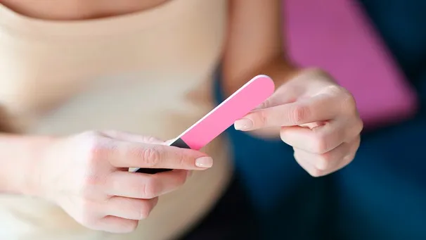 Nahaufnahme einer Frau, die ihre Fingernägel feilt, was die Pflege und das Erscheinungsbild der Nägel beeinflusst.